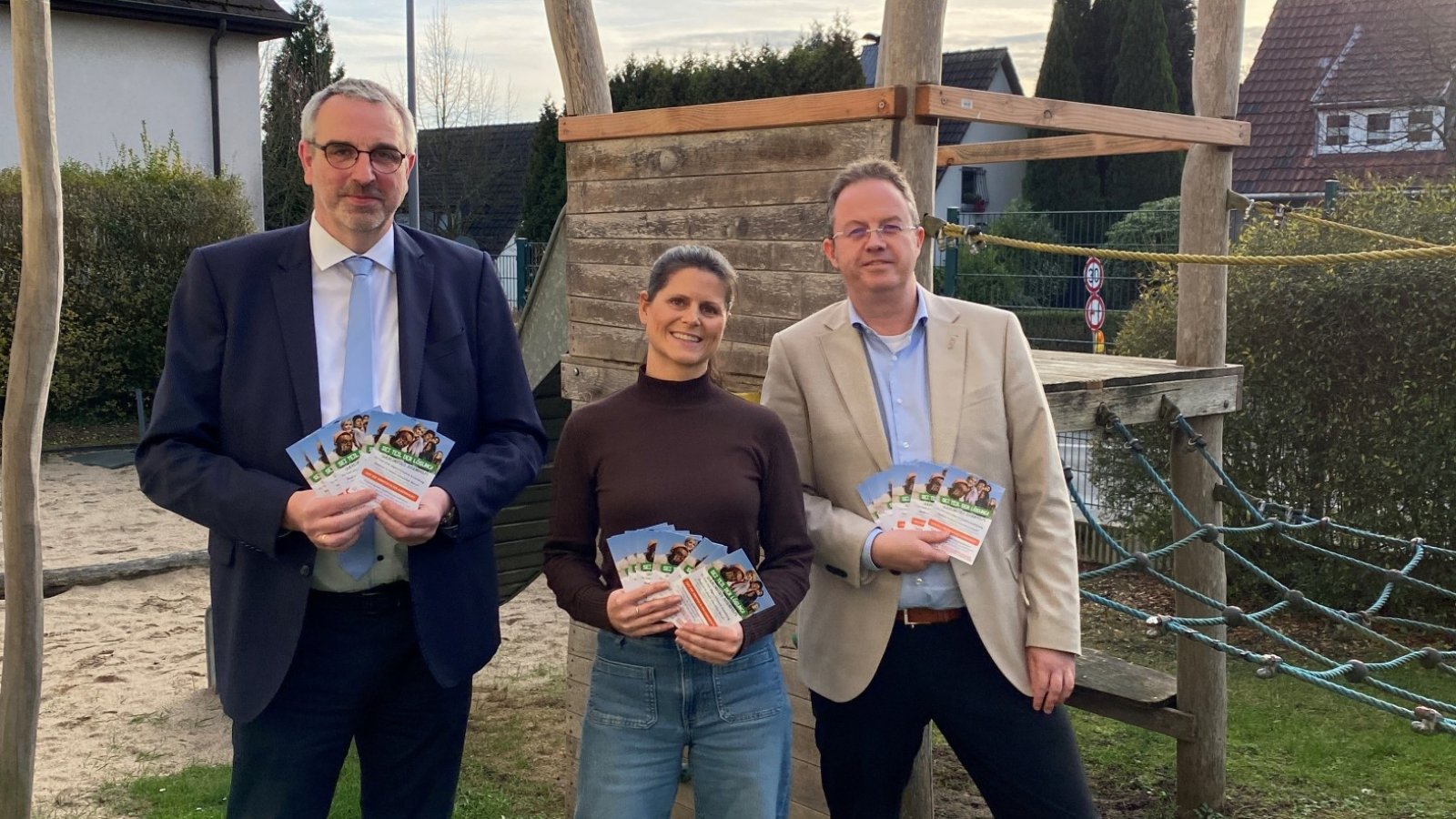 Drei Personen mit Flyern stehen vor einem Klettergerüst