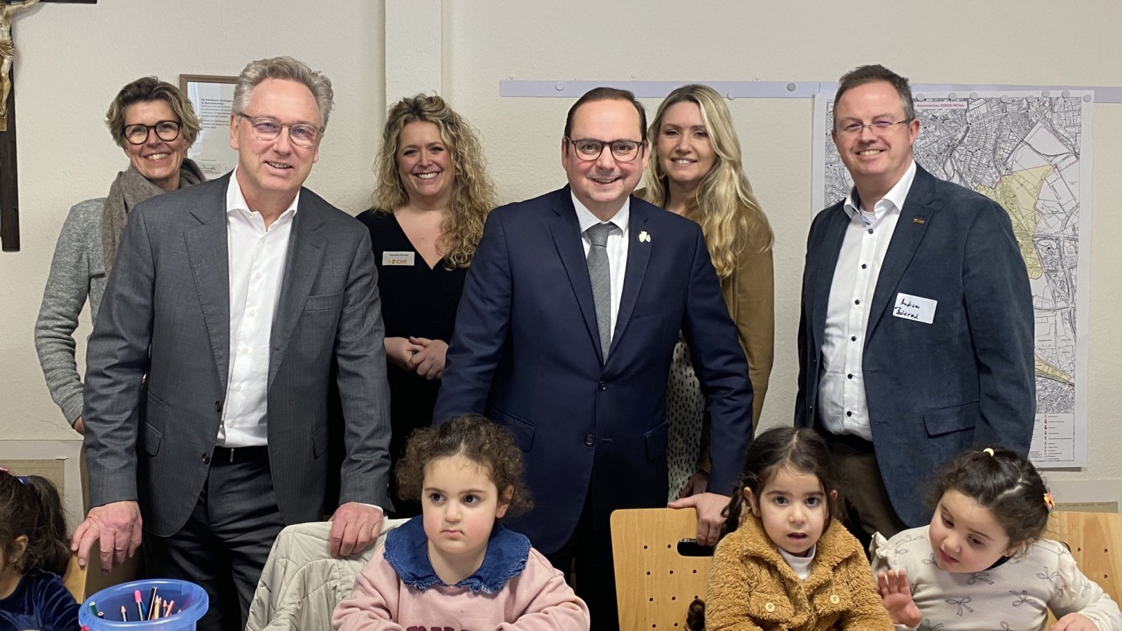 Mehrere Personen stehen nebeneinander, davor Kinder am Basteltisch