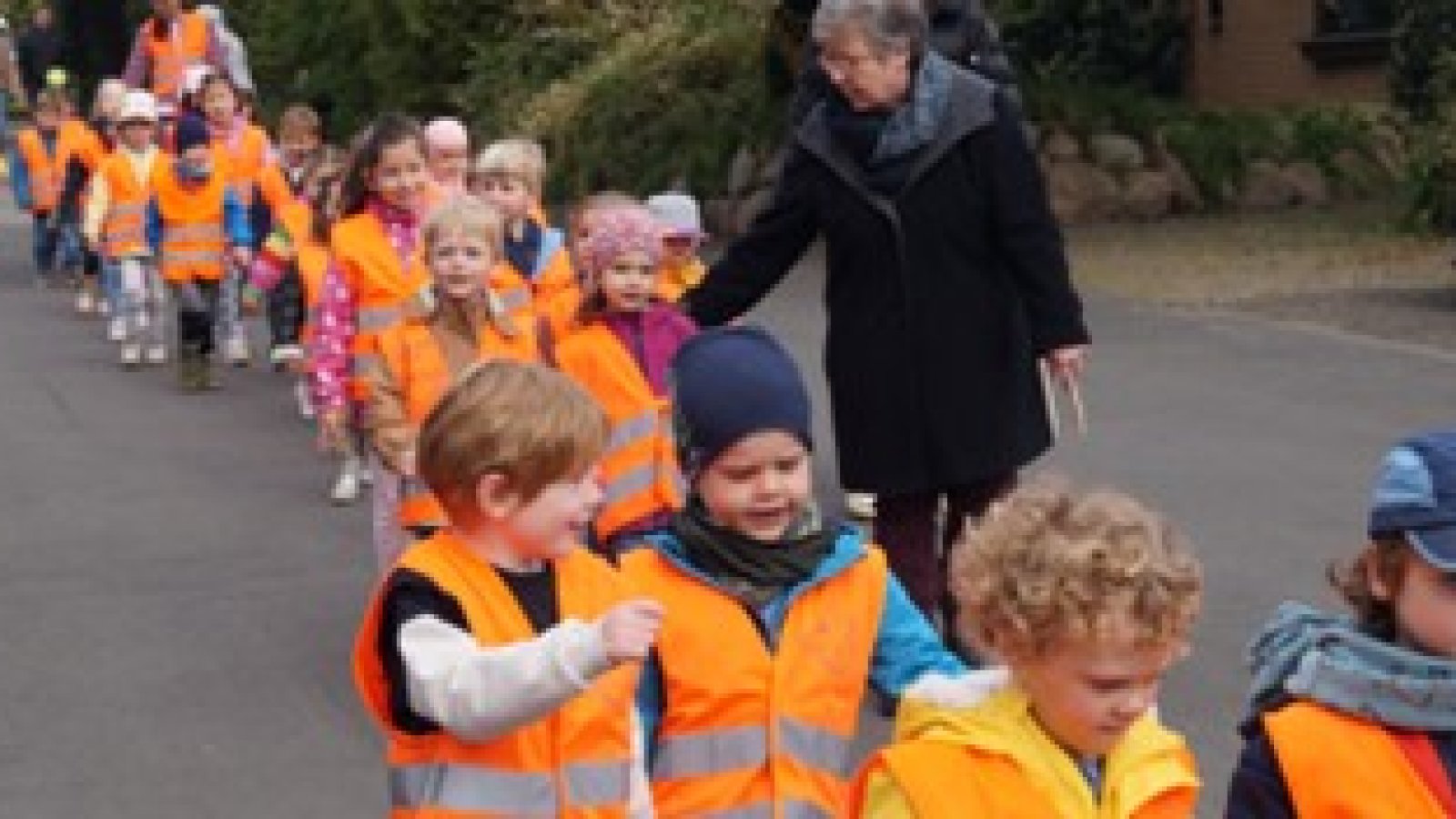 Kinder in orangenen Warnwesten auf dem Weg zum Müll sammeln