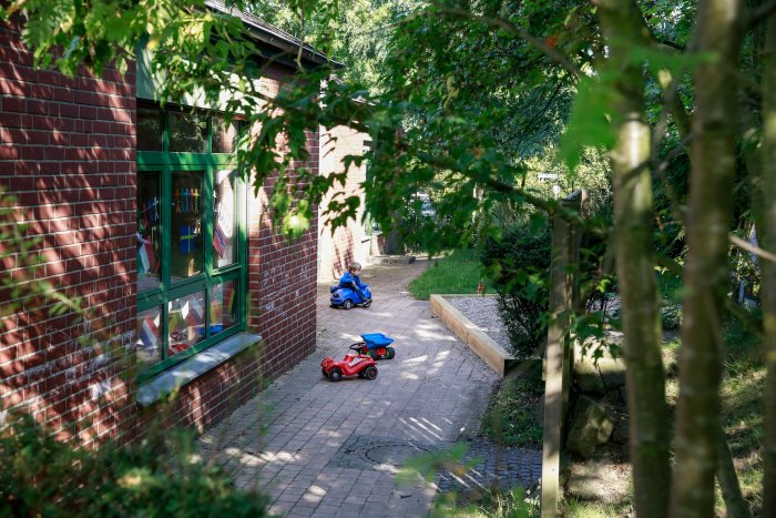 Außengelände des Familienzentrums, links Hauswand, in der Mitte Weg mit Bobbie Cars und rechts Grünfläche. 