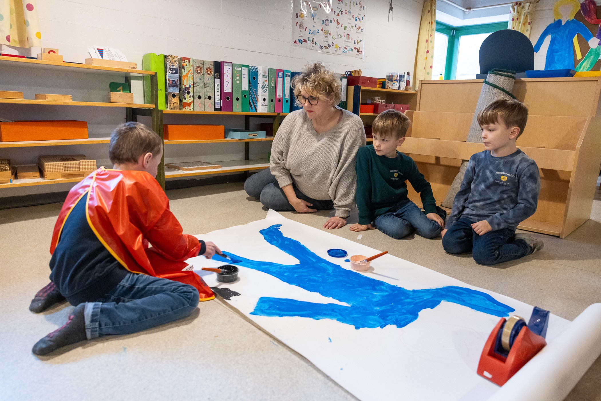 Erzieherin mit Kindern auf dem Boden sitzend beim Malen