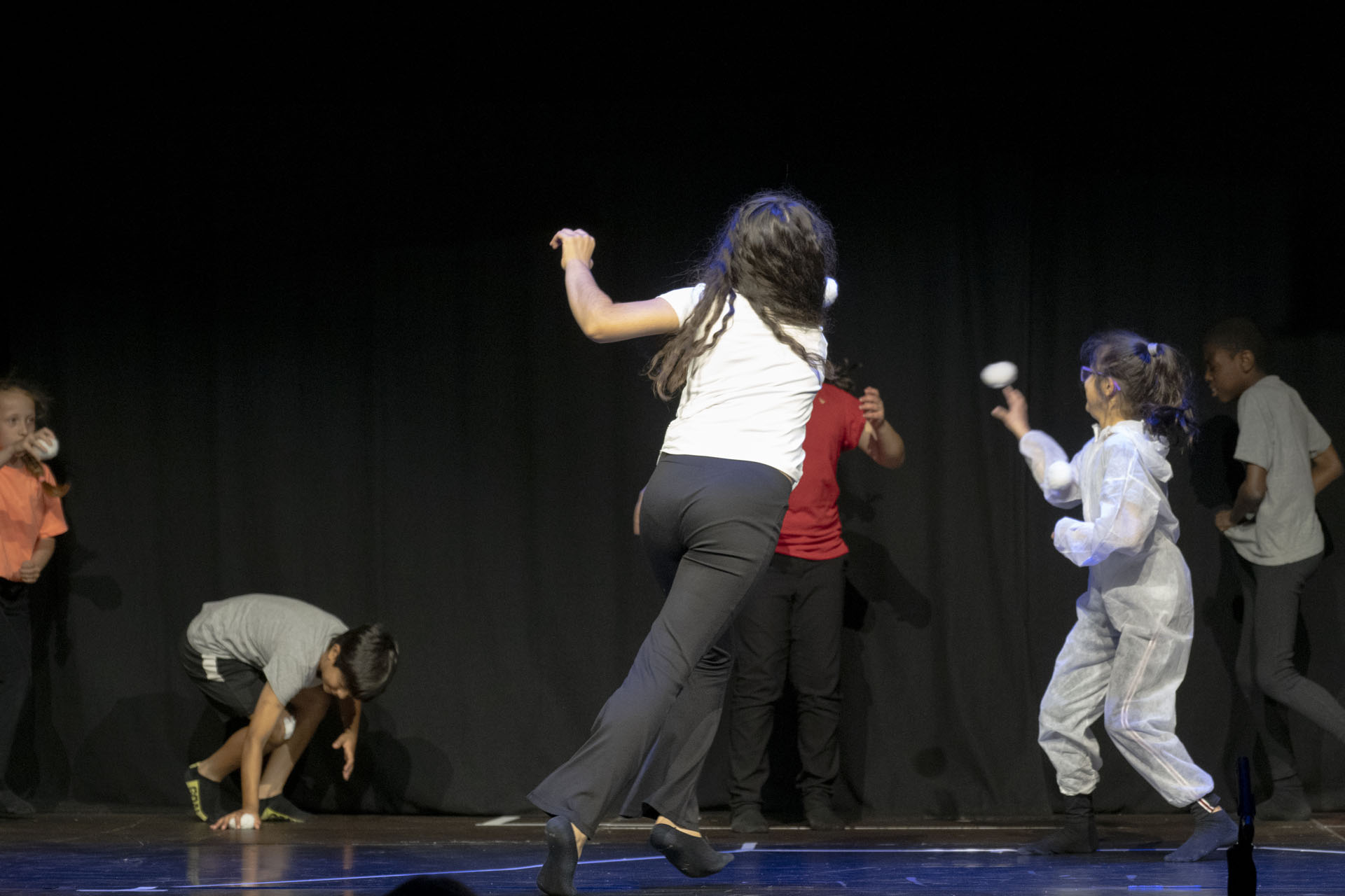 Kinder werfen Ball auf einer Theaterbühne.