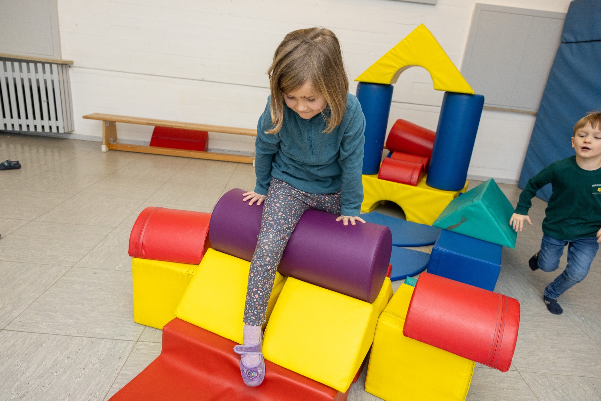 Mädchen beim Klettern in der >Turnhalle über Bauelemente