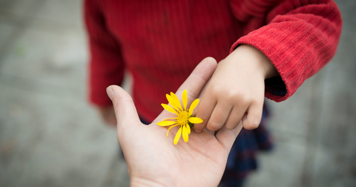Hand Erwachsener und Kind mit gelber Blume