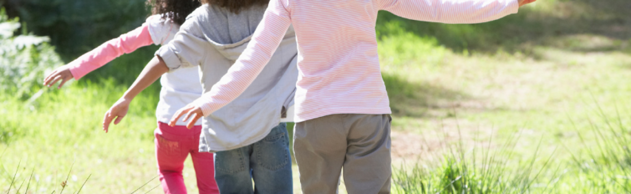 Drei Kinder balancieren auf einem Weg durch eine Wiese.